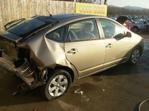 Damaged tan Toyota Prius in a salvage yard with rear-end collision damage.