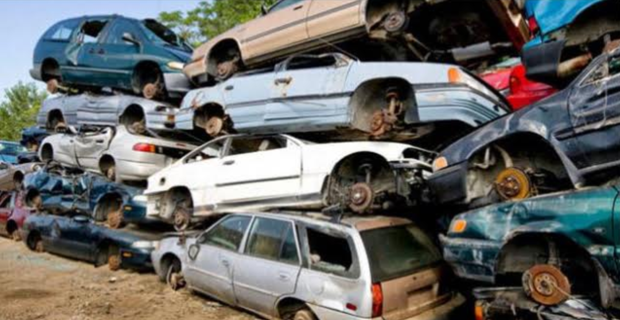 Pile of junked cars, various colors, stacked haphazardly. Wheels missing, setting outdoors.
