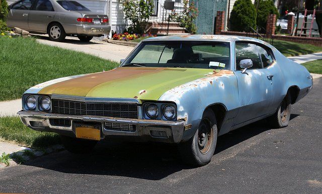 Rusty, vintage Buick Skylark car parked on a street with faded blue and green paint.