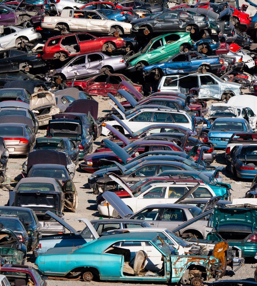 Cars in a junkyard, packed tightly, hoods and doors open. Various colors and conditions.